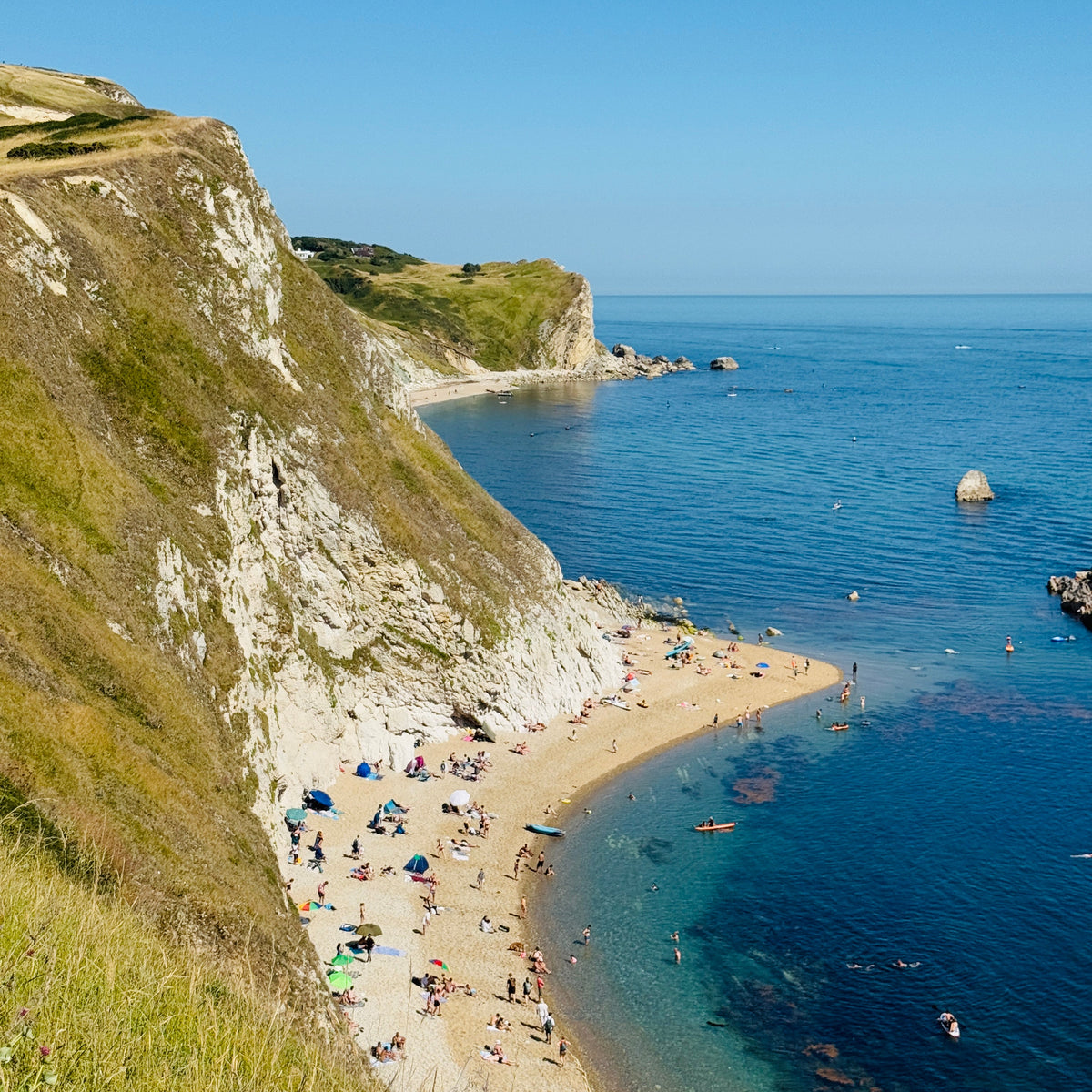 Beach with people and cliffs overlooking the ocean under a clear blue sky